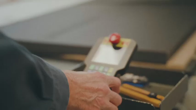 This video showcases the industrial fabrication of custom foam products. It begins with a worker operating a control panel for a CNC router, which precisely cuts intricate shapes into large sheets of dark foam material. Other scenes show automated die-cutting and slitting machines processing foam, followed by workers manually assembling and gluing the cut foam pieces to create custom inserts and protective packaging solutions. The video highlights various stages of foam manufacturing, from automated cutting