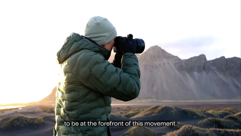 A video introducing NANUK's new 'R' line of eco-responsible protective cases. It showcases the design and development process, emphasizing the use of recycled materials and the company's commitment to reducing carbon footprint by 60% and achieving carbon neutrality. Key scenes include company leaders, designers reviewing blueprints, manufacturing in a warehouse, durability testing (dropping, water resistance), and the cases in real-world outdoor settings like forests and mountains, demonstrating their robus